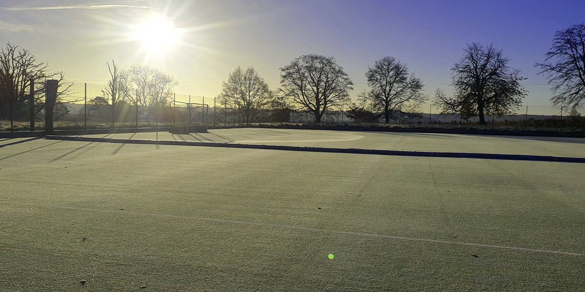 Frosty Green Hockey Pitch with Sun shining over it, trees in a silhouette 